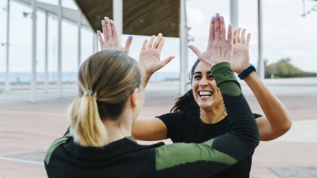 Two women in sportswear high five in the park