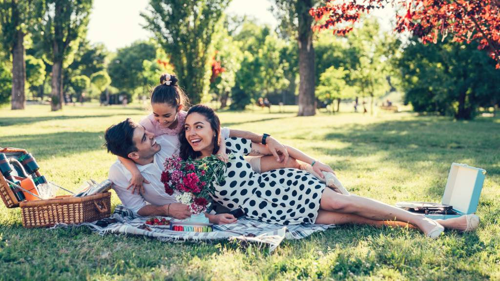 Family of three in the park with Valentine's Day roses and picnic