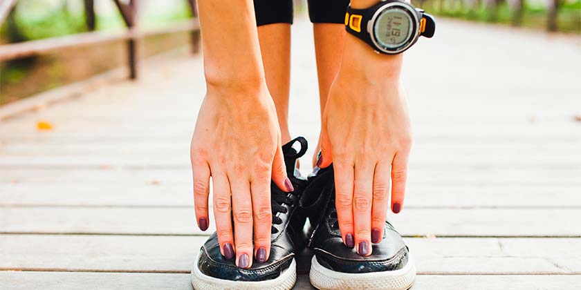 Woman's hands stretching down to her shoes wearing running sneakers