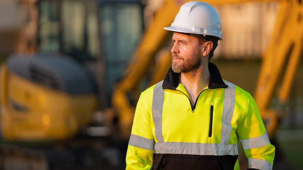 Construction worker wearing a hard hat standing in front of a digger