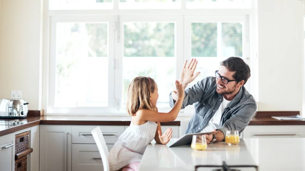 Father and young daughter high five while sitting at the breakfast table. 