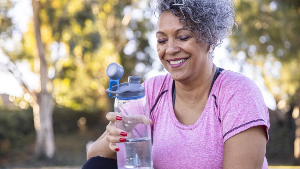 A mature woman in a pink sports top holds a water bottle. 