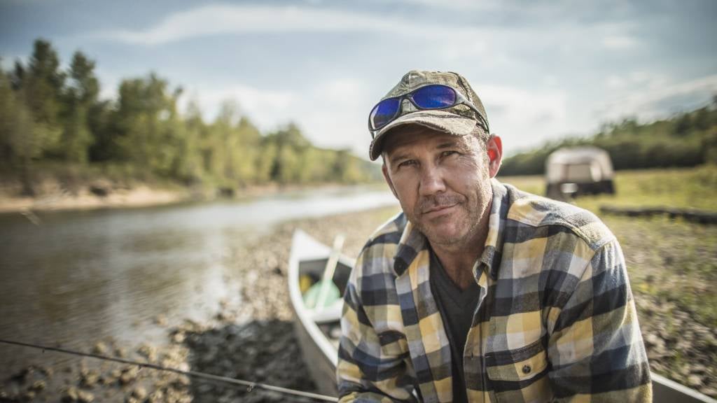 Man in his fifties looks wistful while sitting near a lake and canoe