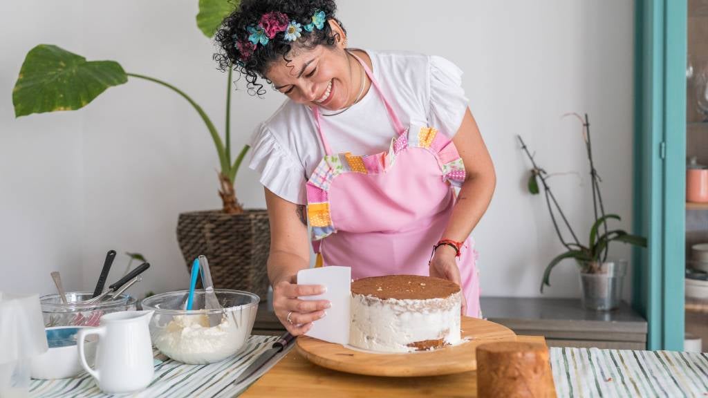 A smiling woman puts icing on a cake