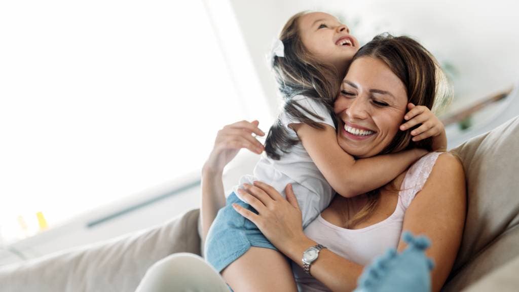 Mother and daughter smiling and hugging on a sofa 