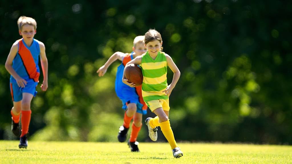 Kids playing Aussie rules football on a sunny day