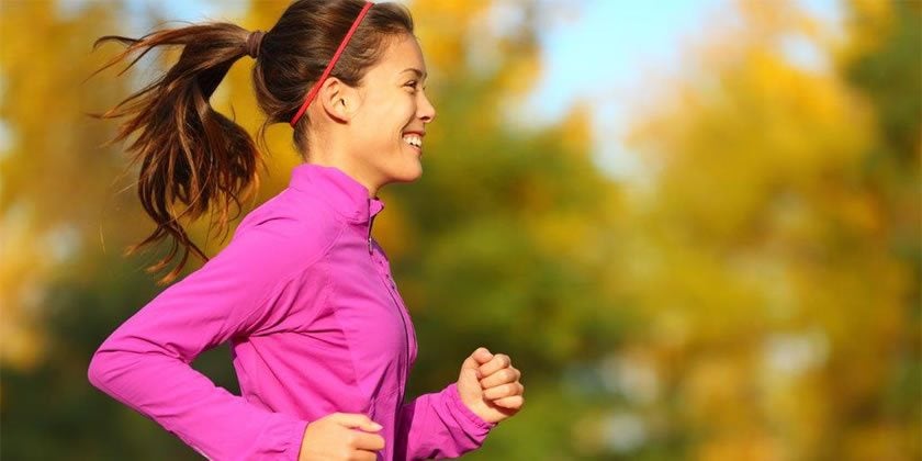 Woman running in purple tracksuit top with brown hair in ponytail 