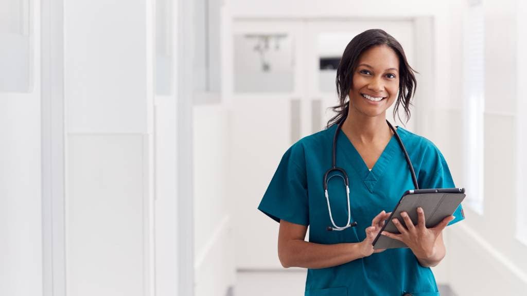 Nurse in teal scrubs holding a tablet in a hospital
