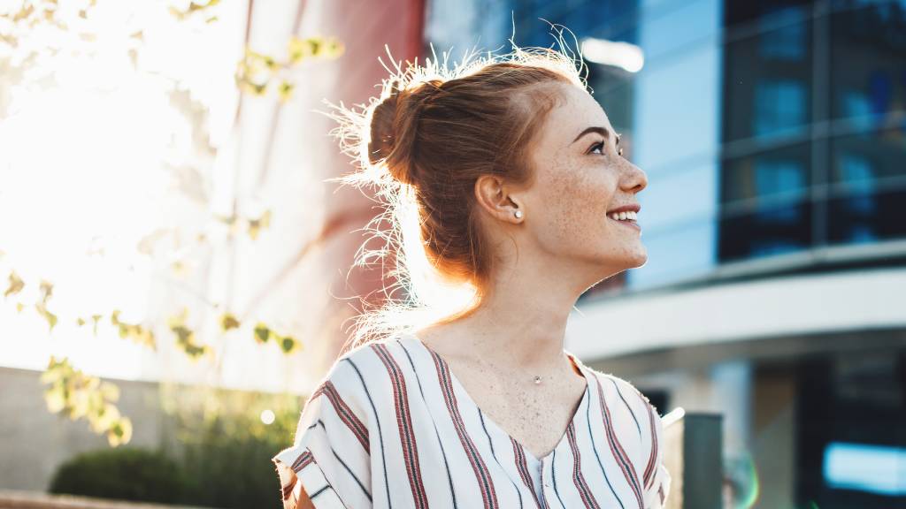 cheerful young woman with freckles and red hair posing against the sunshine