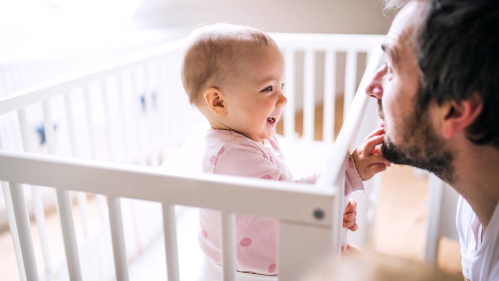Bearded modern father smiling at his young baby in a cot
