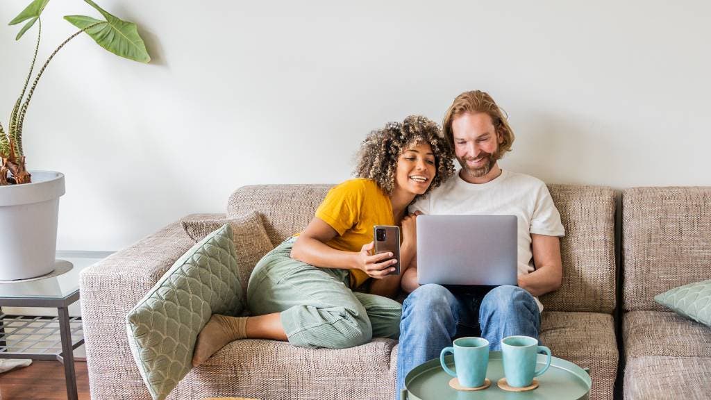Young couple relax on their sofa while looking at a laptop