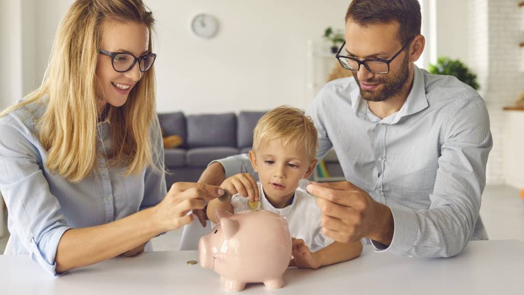 Mother, father and young son put money into a piggy bank. 