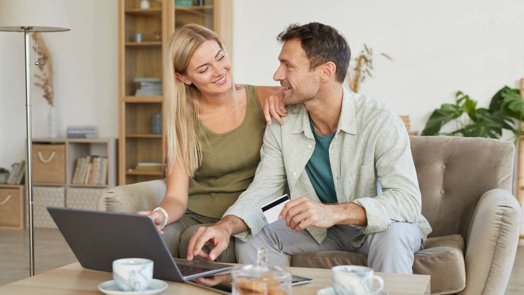Young couple at home smile at each other and work on a laptop. 