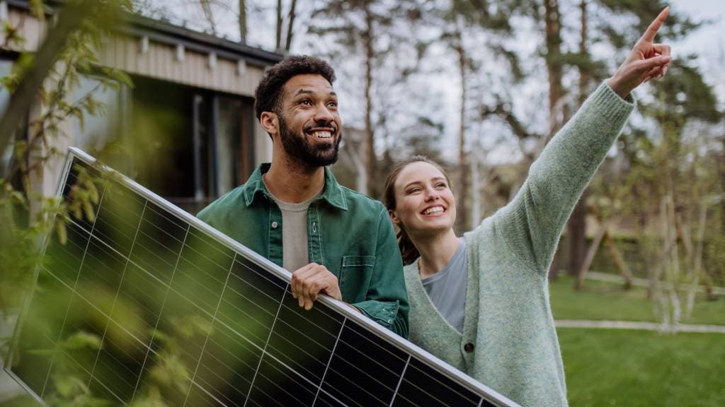 A smiling couple carrying a solar panel in their yard