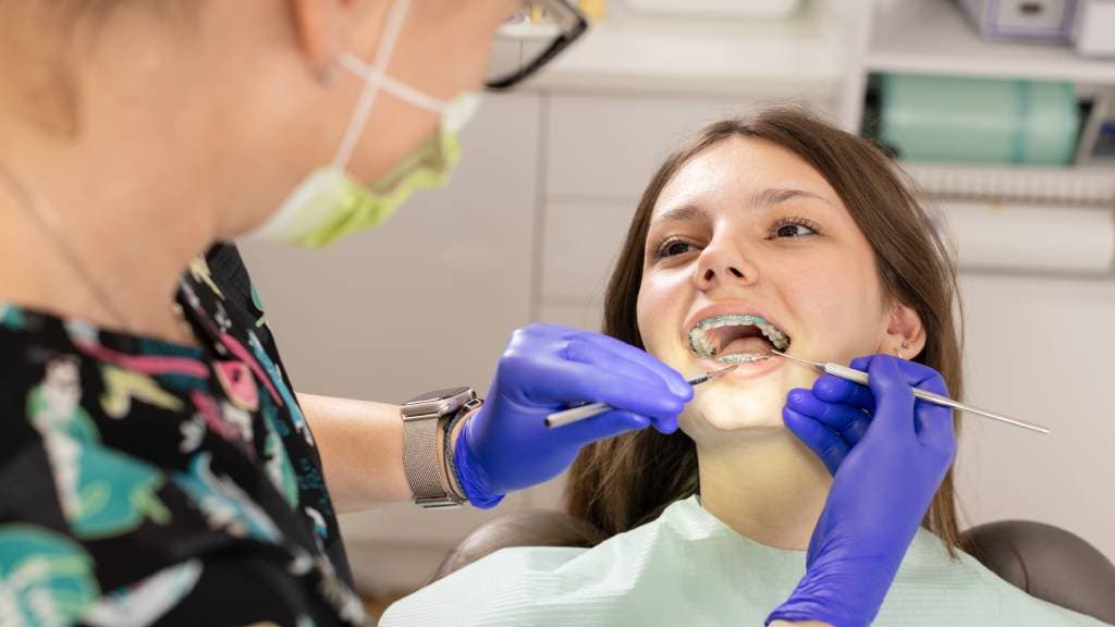 Young girl wearing braces gets her teeth checked by a dentist