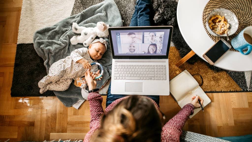 Working mother with baby, laptop, smartphone and snacks, pictured from above. 