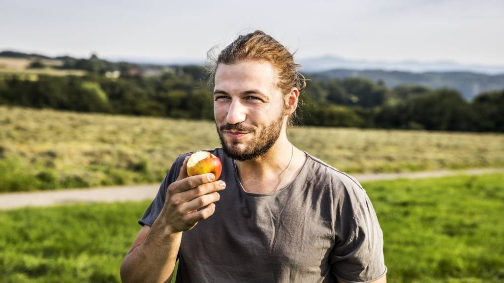 Young man in his 20s eating an apple in rural landscape