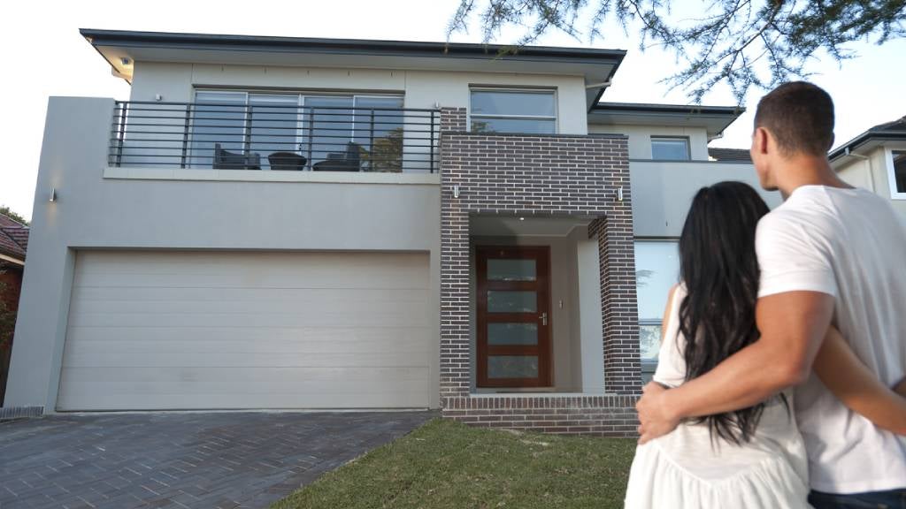 Couple hugging while standing outside in front yard looking at home.