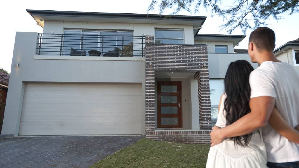 Couple hugging while standing outside in front yard looking at home.