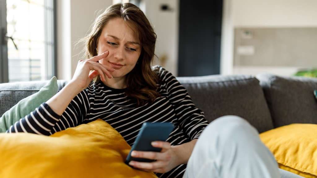 A woman is scrolling on her phone while sitting on a couch. 