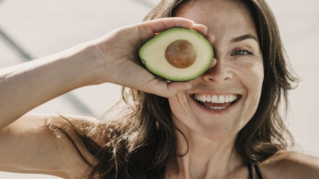 Happy woman in her 40s posing with an avocado