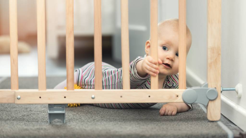 Small baby in onesie shown behind baby gate