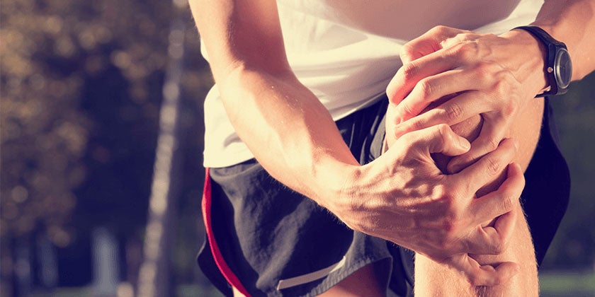 Male runner holding knee with both hands and stretching 