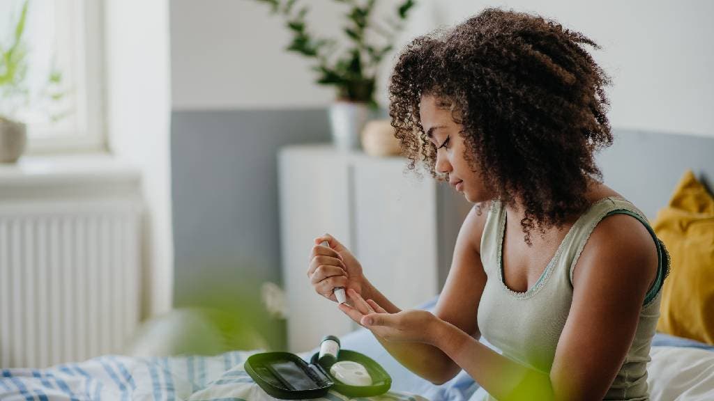 Woman testing her blood sample on a blood sugar meter at home. 