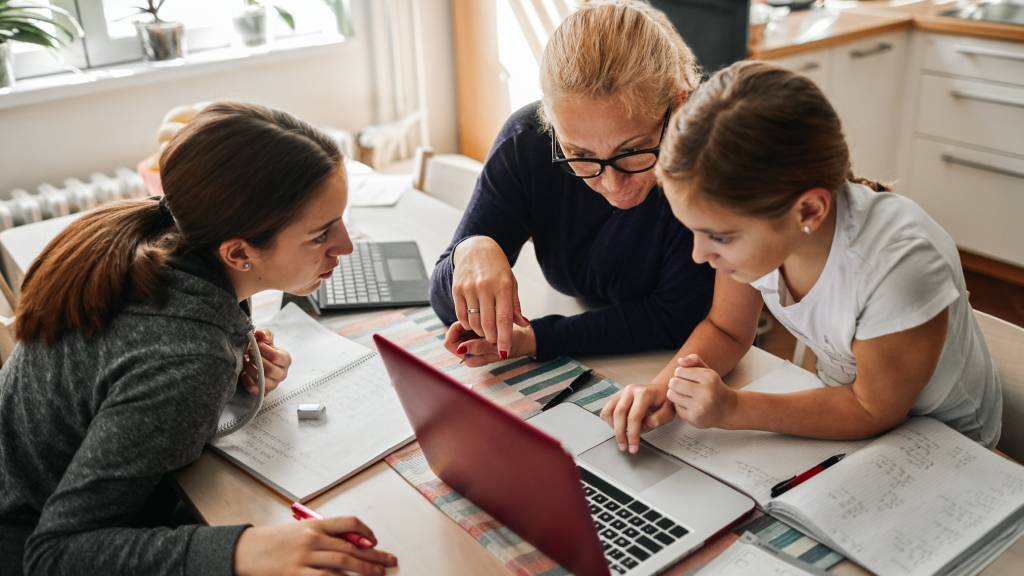 Young girl does homework on laptop with mother and grandmother