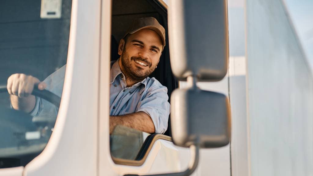 Person smiling from the driver's seat of a white delivery truck