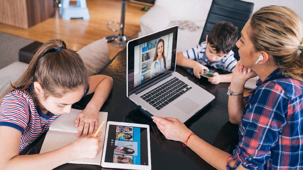 Mother trying to talk with doctor on laptop while watching two kids staying home