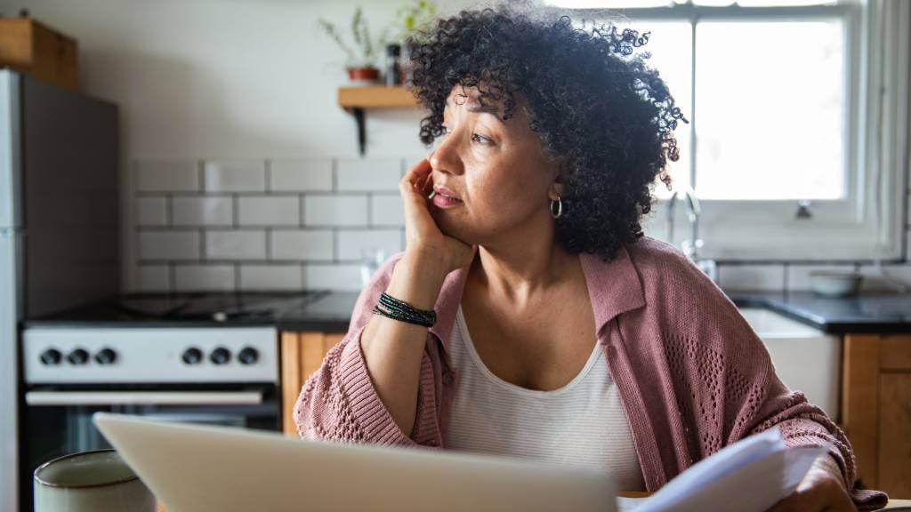 Woman looks out of her window whilst working on her laptop