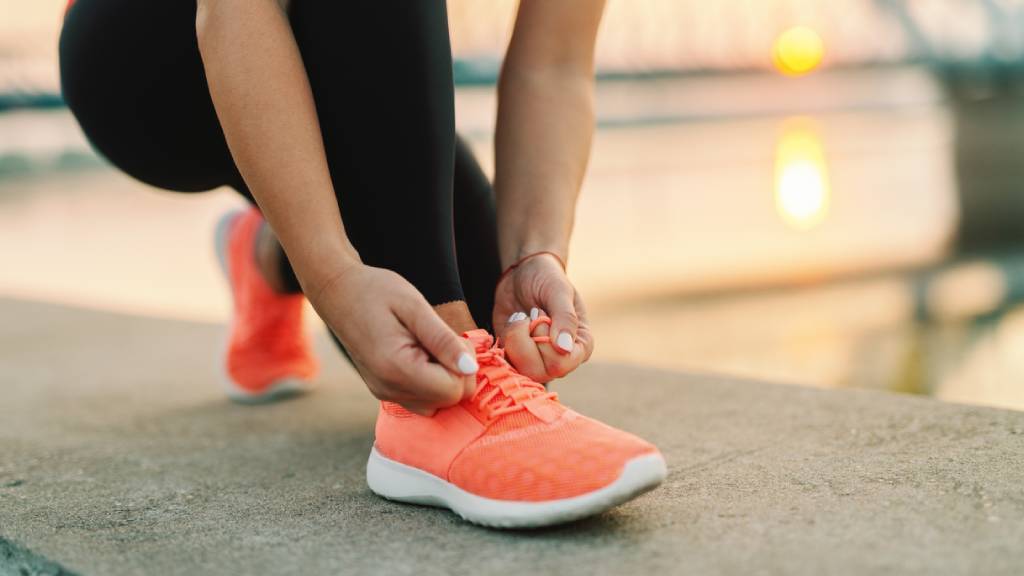 Woman in black activewear tights ties up bold orange running shoe 