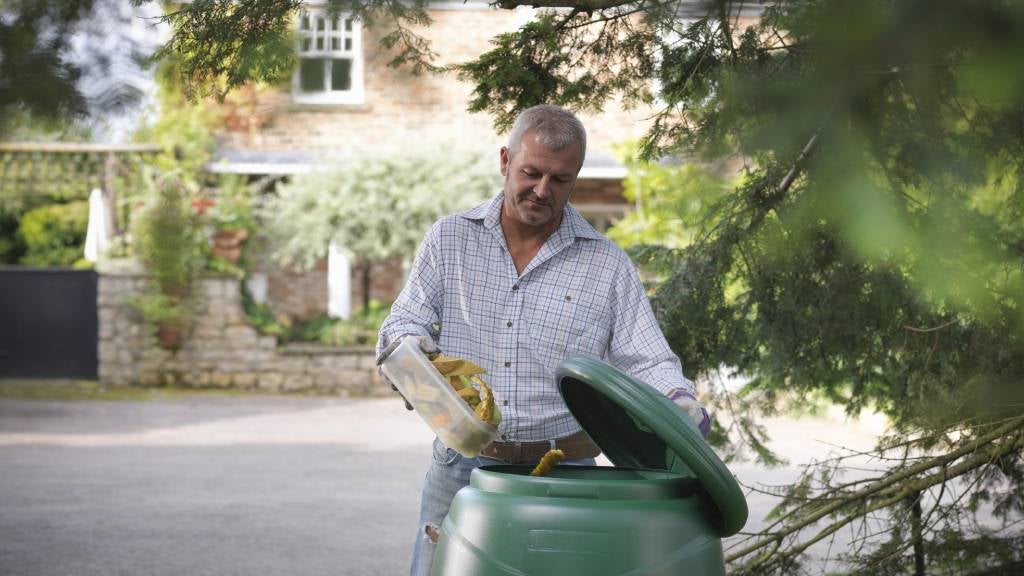Man puts scraps into compost bin with a lid 