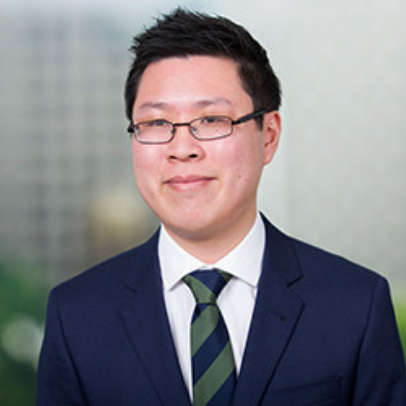 Business man looking off camera, smiling with black hair and glasses and suit wuth green and blue tie.