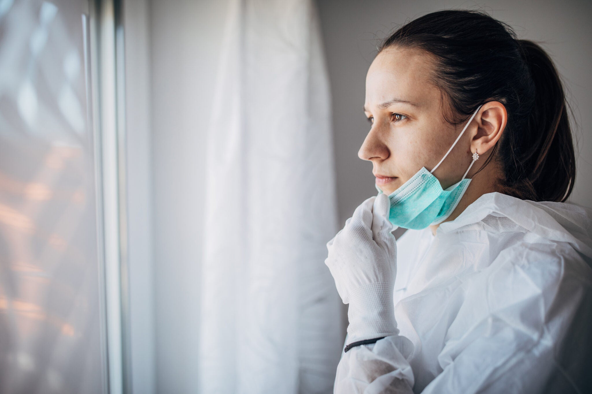 Worried doctor in protective suit, looking through the hospital window.