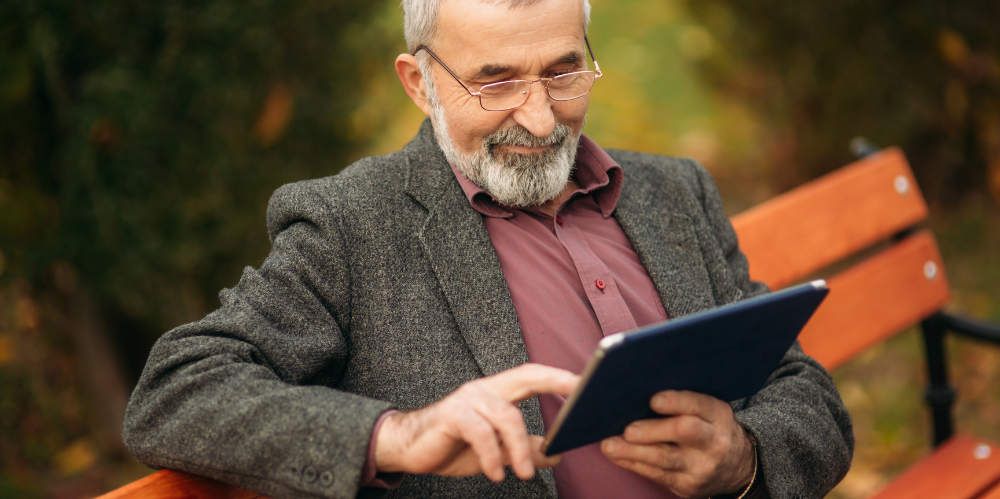 Man sitting on bench looking at a tablet computer.