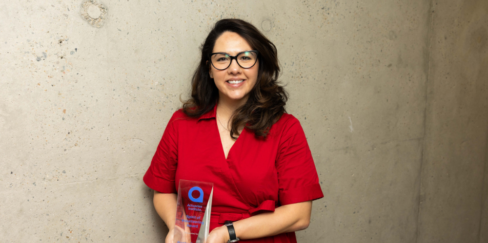 Female in a red dress, black hair shoulder length and black round glasses, smiling at camera and holding a glass trophy