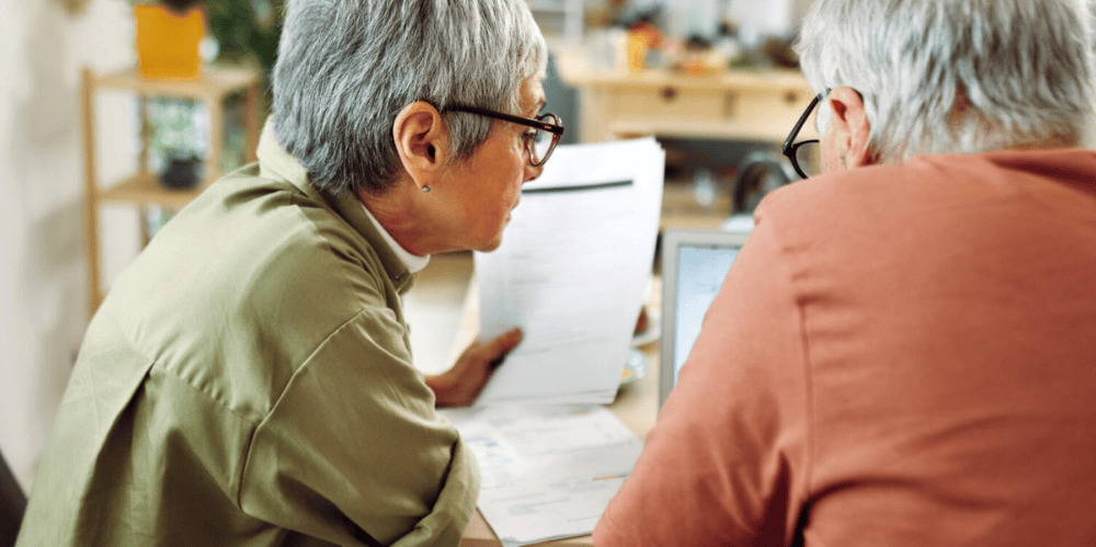 Elderly couple look inquisitively at documents together