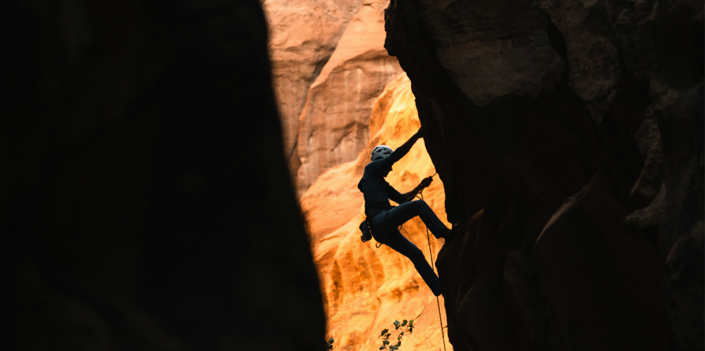 A photo of a person rock-climbing a red and orange cliff. They are wearing appropriate safety gear. 
