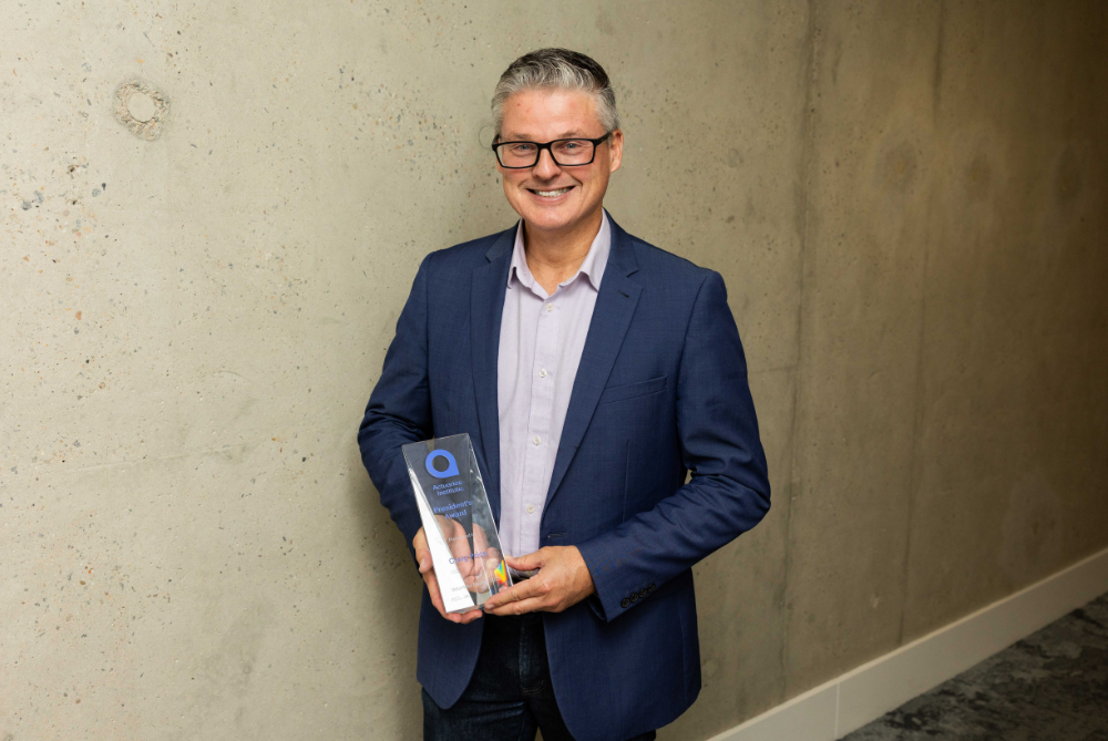 Business man in grey suit, holding a trophy and smiling 