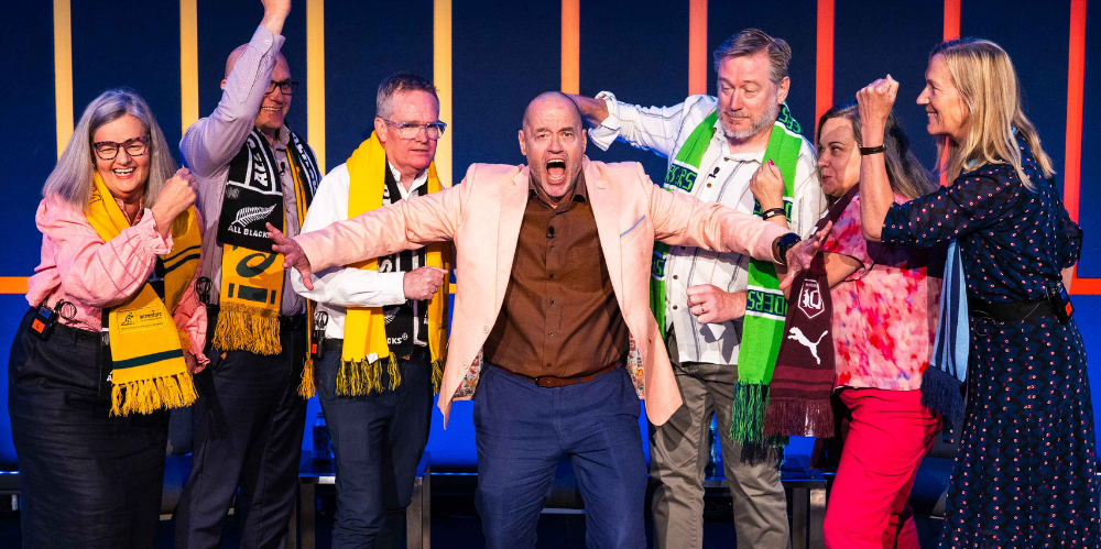 Group of speakers onstage with MC making arguing hand gestures - IDSS 2025