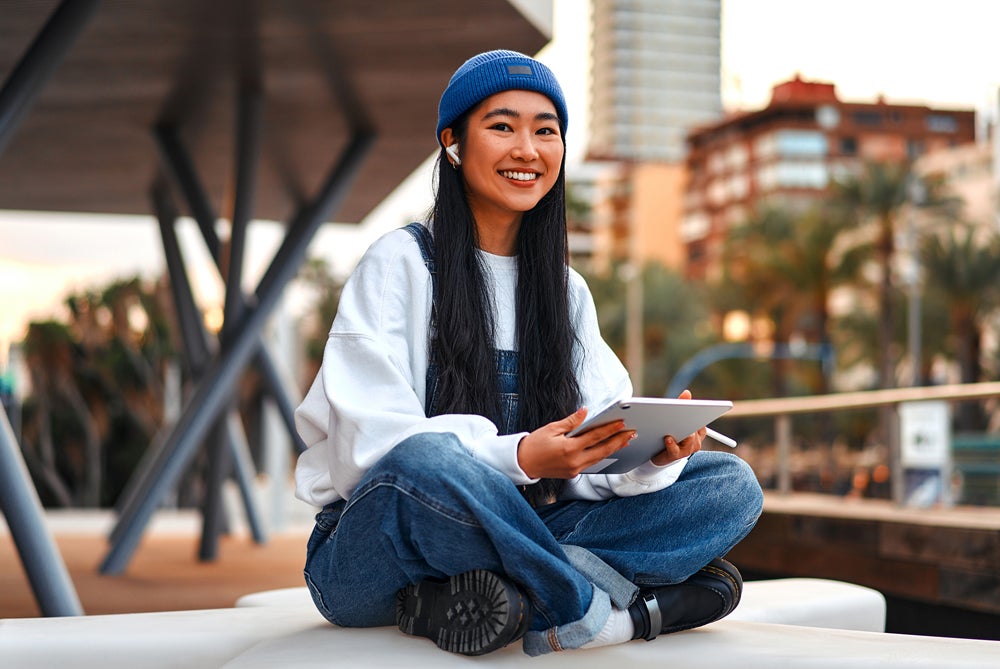 Girl with long black hair wearing beanie and holding iPad