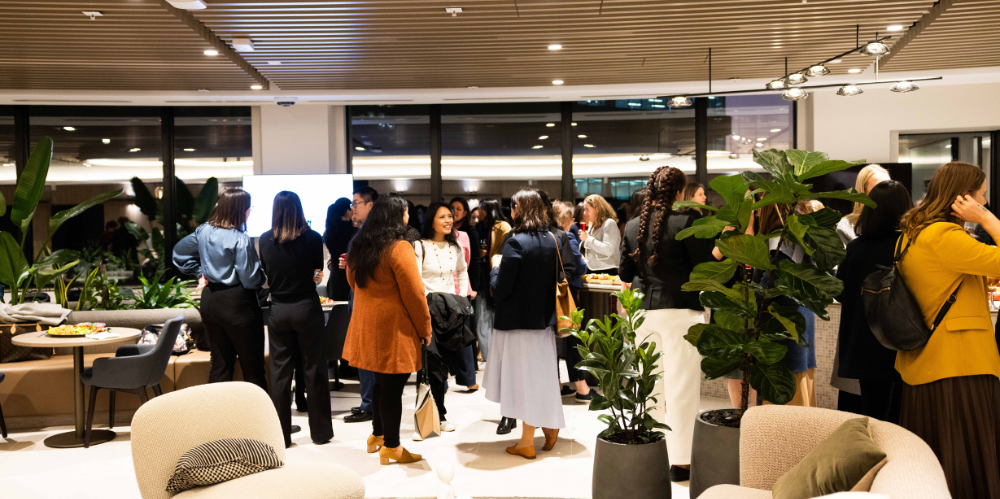 Conference room with people standing around chatting, with lounges, plants and lighting