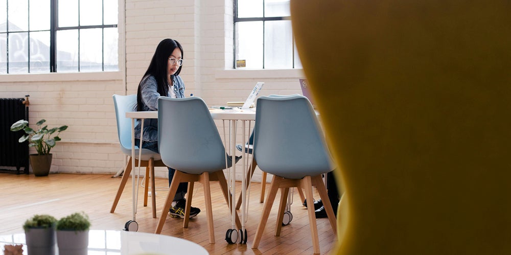 Woman with black hair sitting at a desk working on a laptop