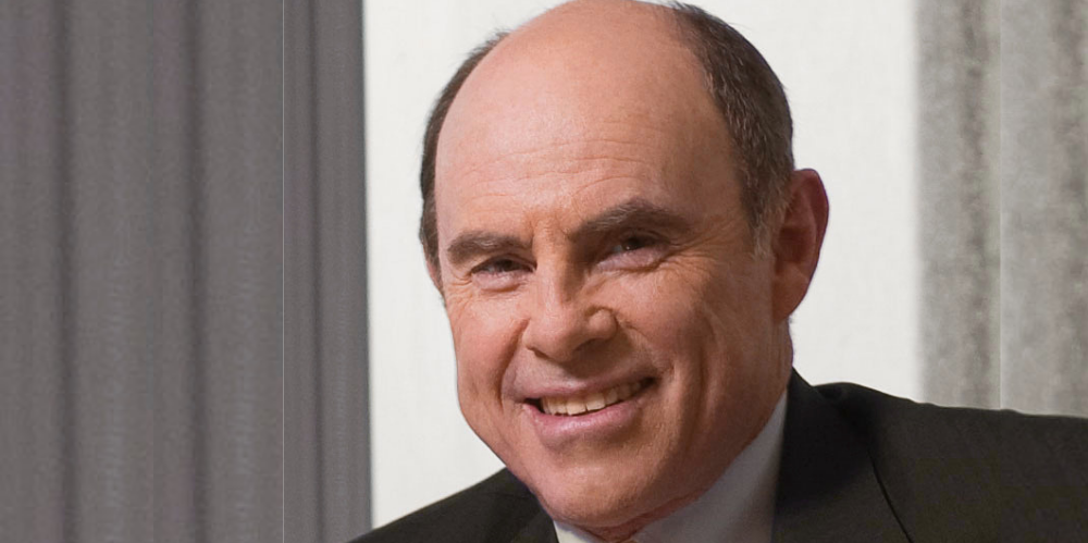 Business man smiling at camera wearing dark suit and yellow tie, head shot photo.