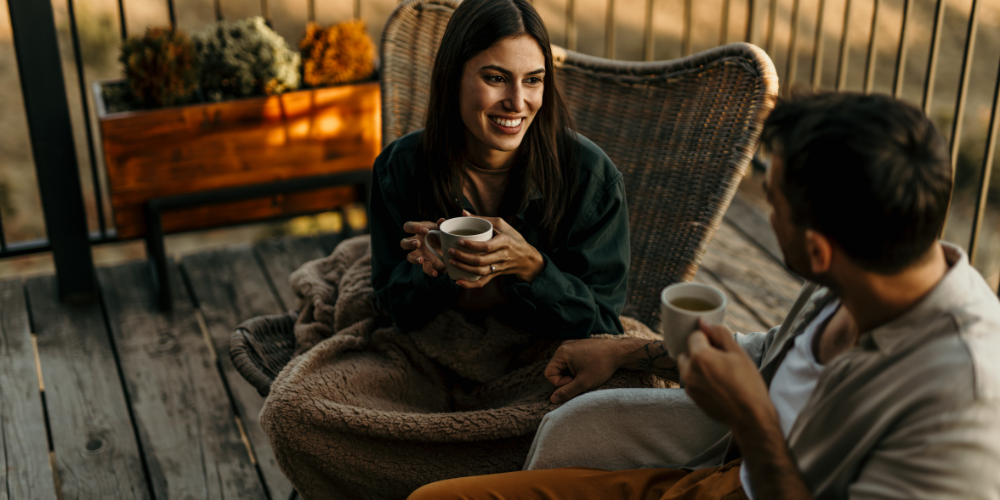 A women and man sitting on an outside deck talking. 