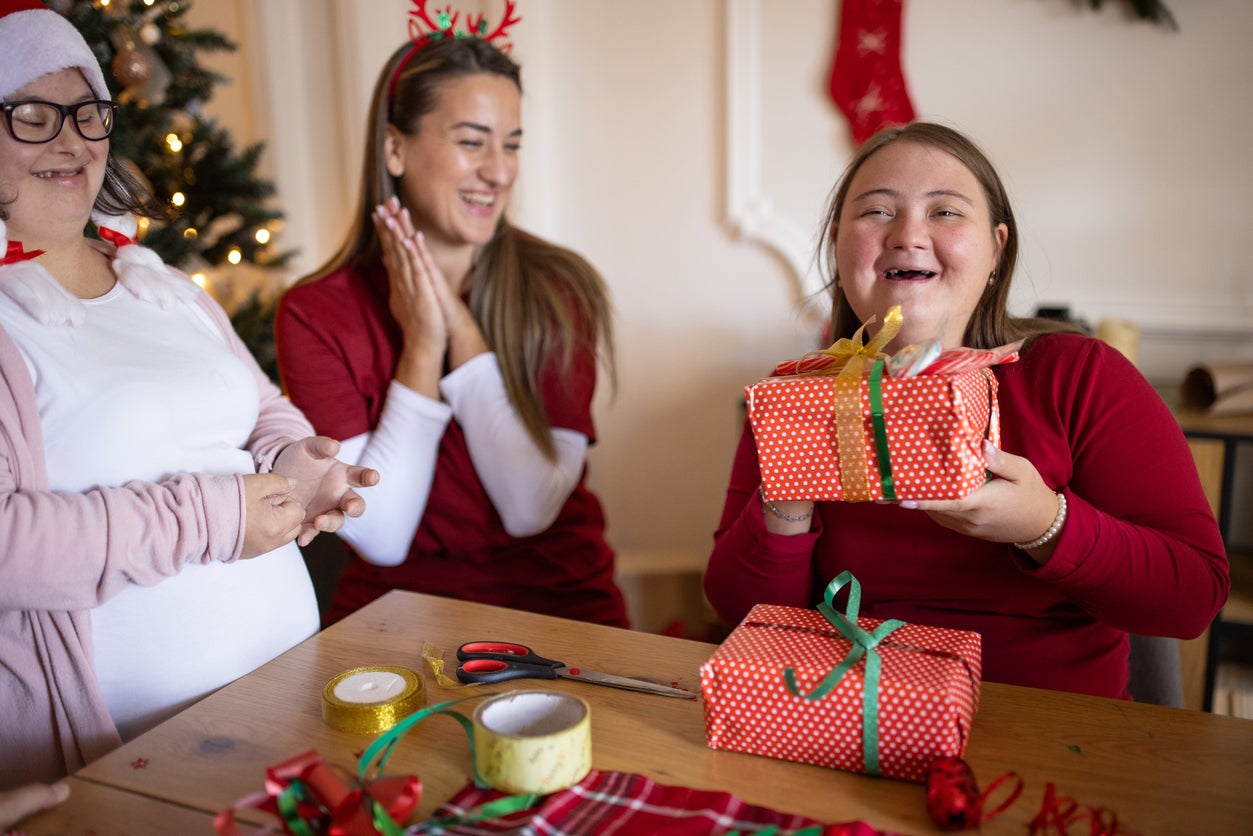 People with Down syndrome wrapping gifts together in the living room of a house with the help of their friends
