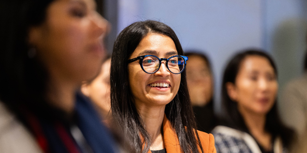 Business women at an events smiling wearing black glasses and orange jacket