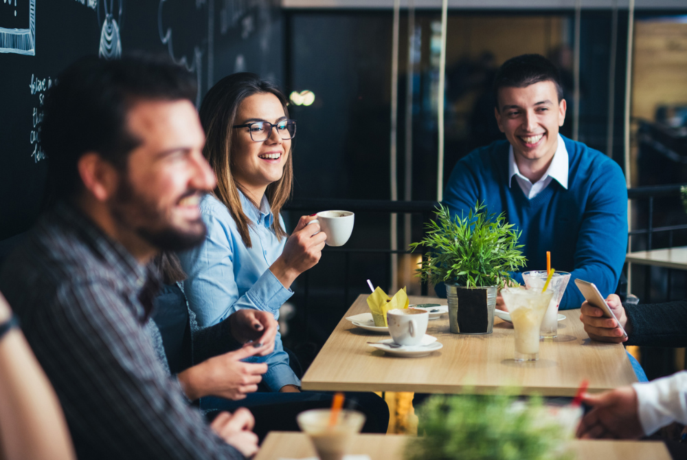 Three people sitting around having coffee smiling at someone off shot